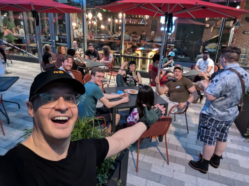 me gesturing at 3 tables of people behind me outside under umbrellas in the boston area.