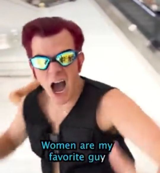 planet of the bass parody of europop meme song young white man with shiny goggles red dyed medium length hair and black sleeveless vest singing intensely women are my favorite guy.