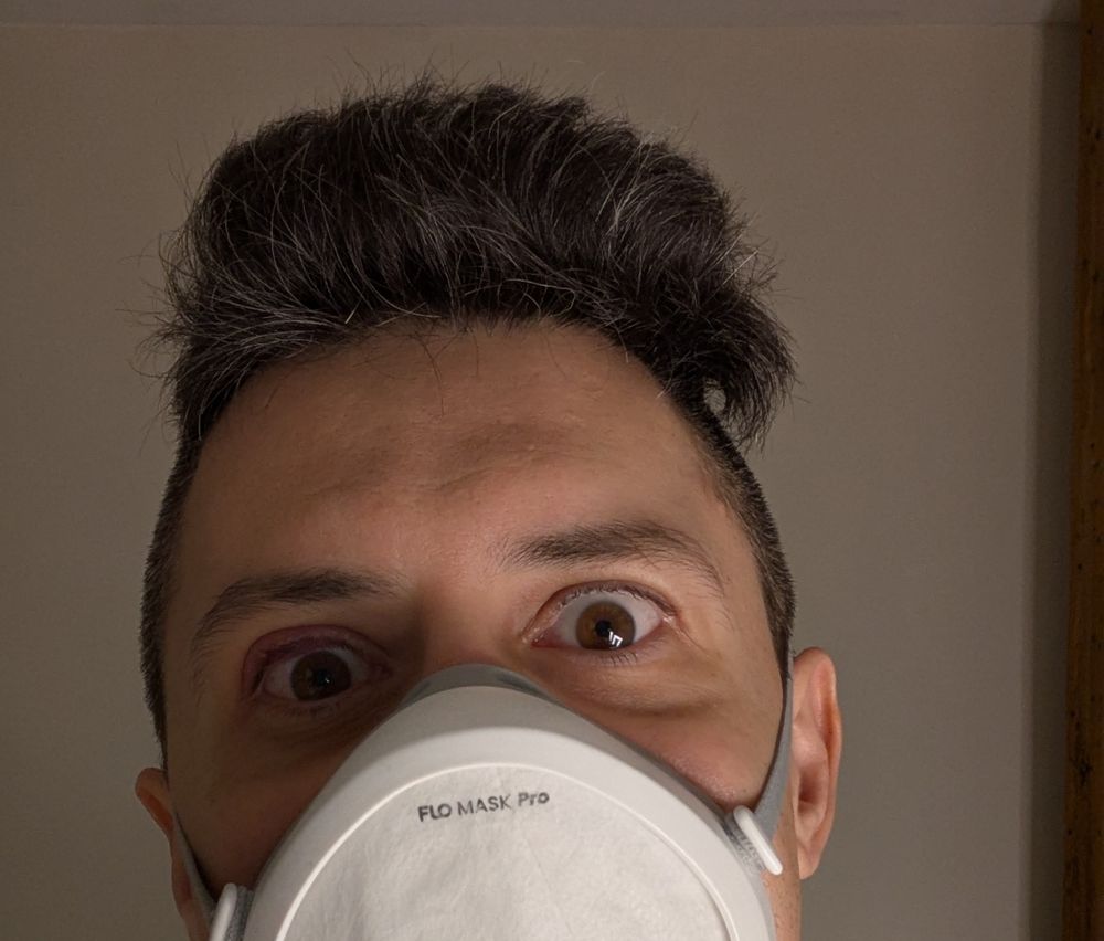 me in flo mask in mirror, very short hair on sides and top hair is standing up tall tipping to a side, I'm doing wild eyed glare, lit from the side low.