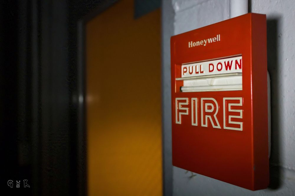 Fire alarm pull station next to a door in the dark.