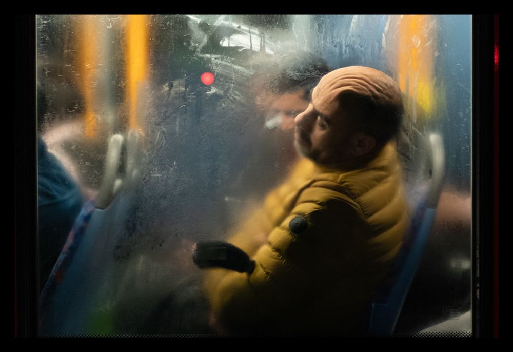 Photo of a man resting his head against a foggy bus window, forming wavy wrinkles.
