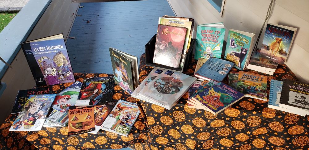 Books displayed on tables which are draped in an orange and black Halloween pumpkin tablecloth.