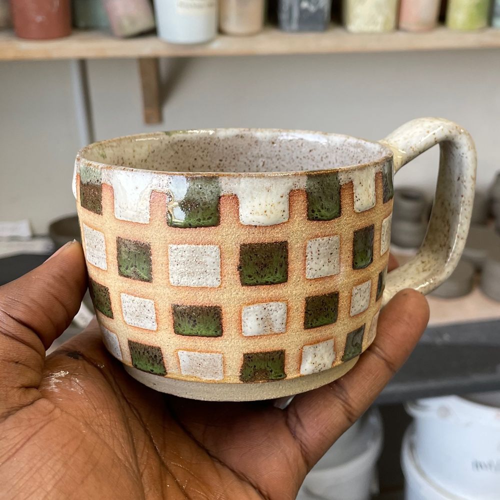 A stoneware mug, glazed in a white and green checkerboard pattern