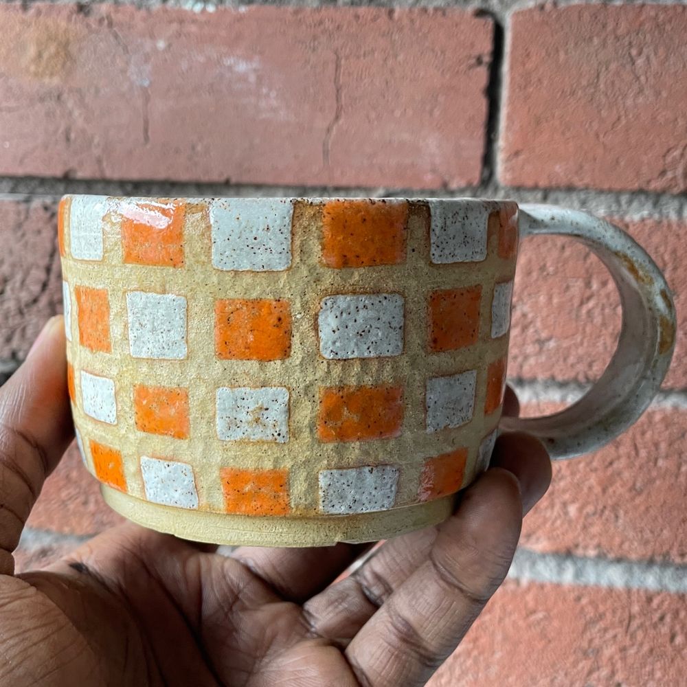 A stoneware mug, glazed in a white and orange checkerboard pattern