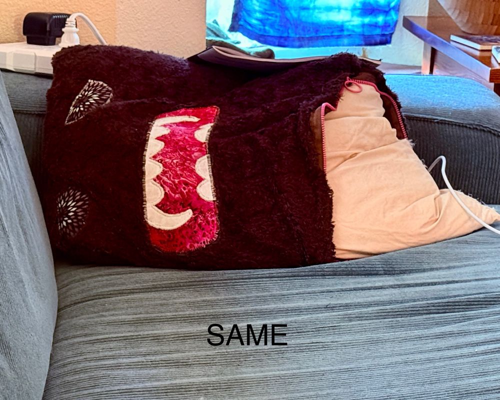 A forlorn handmade domokun pillowcase with a burst zipper and its stuffing coming out lies on its side on a blue couch. The word "same" is printed below