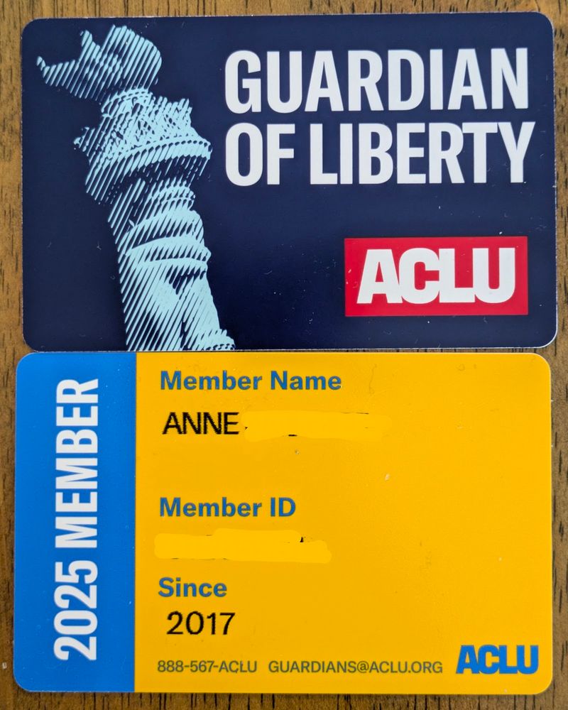 Two sides of a membership card are pictured. The front side has a picture of the Statue of Liberty's torch and the words "Guardian of Liberty" in white against a dark blue background, and the ACLU logo in white on a red background. The back side has a blue bar running vertically along the left edge with the words "2025 Member" in white; the rest of the back side has the words "Member Name", "Member Number", and "Since" in blue on a yellow background, as well as the ACLU logo, website, and toll-free number, also in blue. The member's first name and the year 2017 are printed in black under the headings "Member Name" and "Since", respectively; the member's last name and ID number have been concealed.