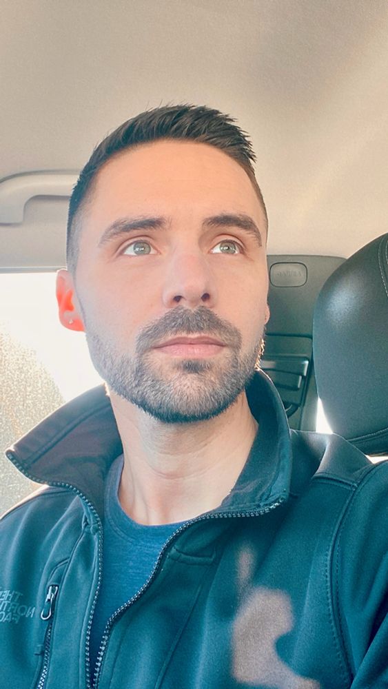 A man with light green eyes in the cab of a sunlit car. 