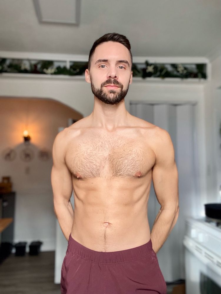 Shirtless man standing with hands clasped behind his back. 