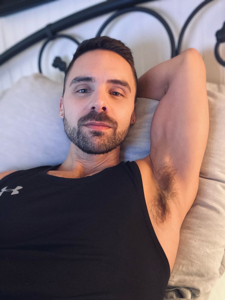 Man wearing a tank top lying in bed with hand resting behind his head.