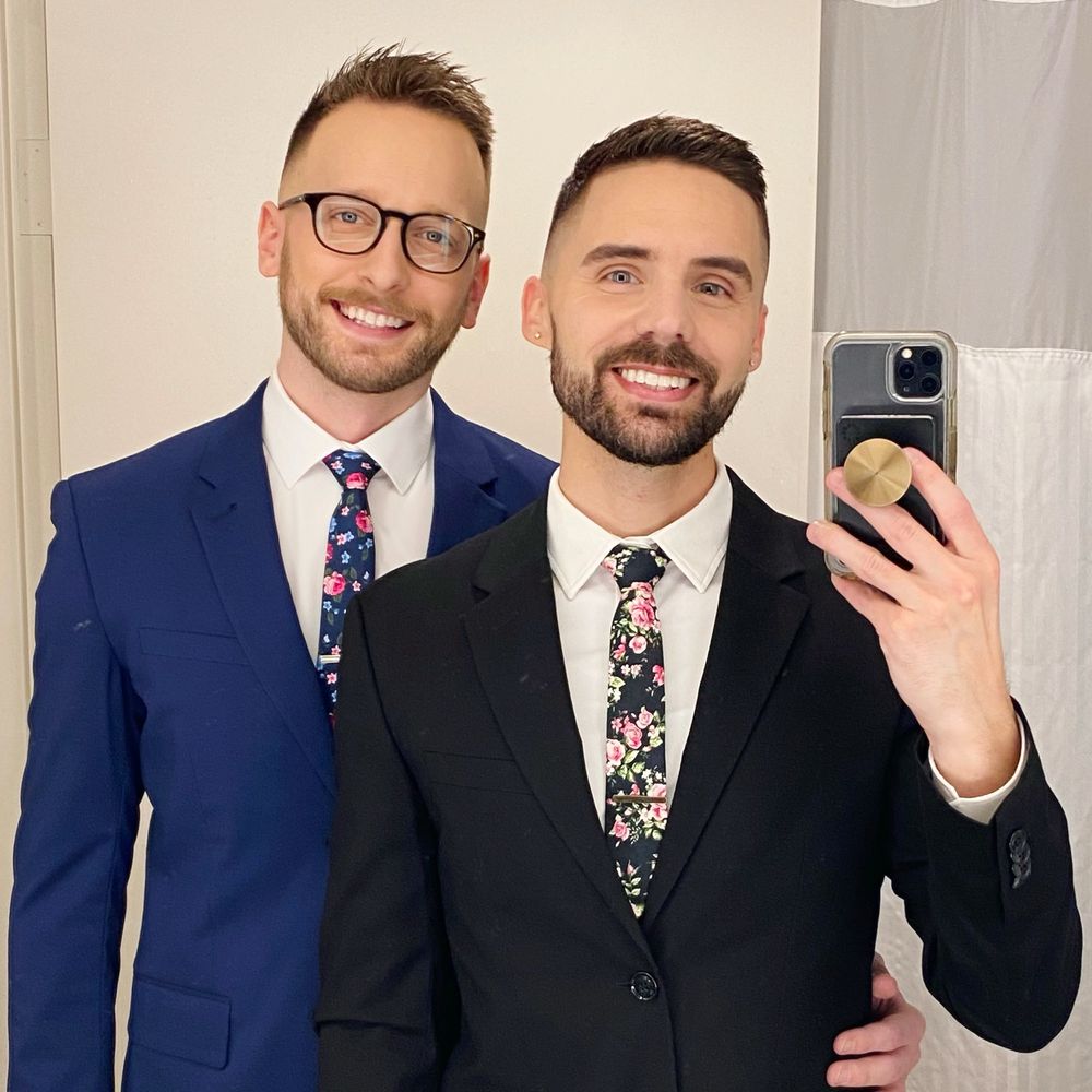 Two mean in suits and floral neckties taking a selfie together. 