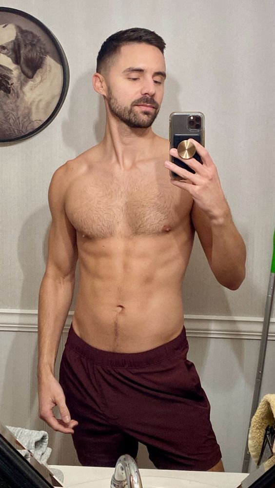 Shirtless man taking a bathroom mirror selfie.