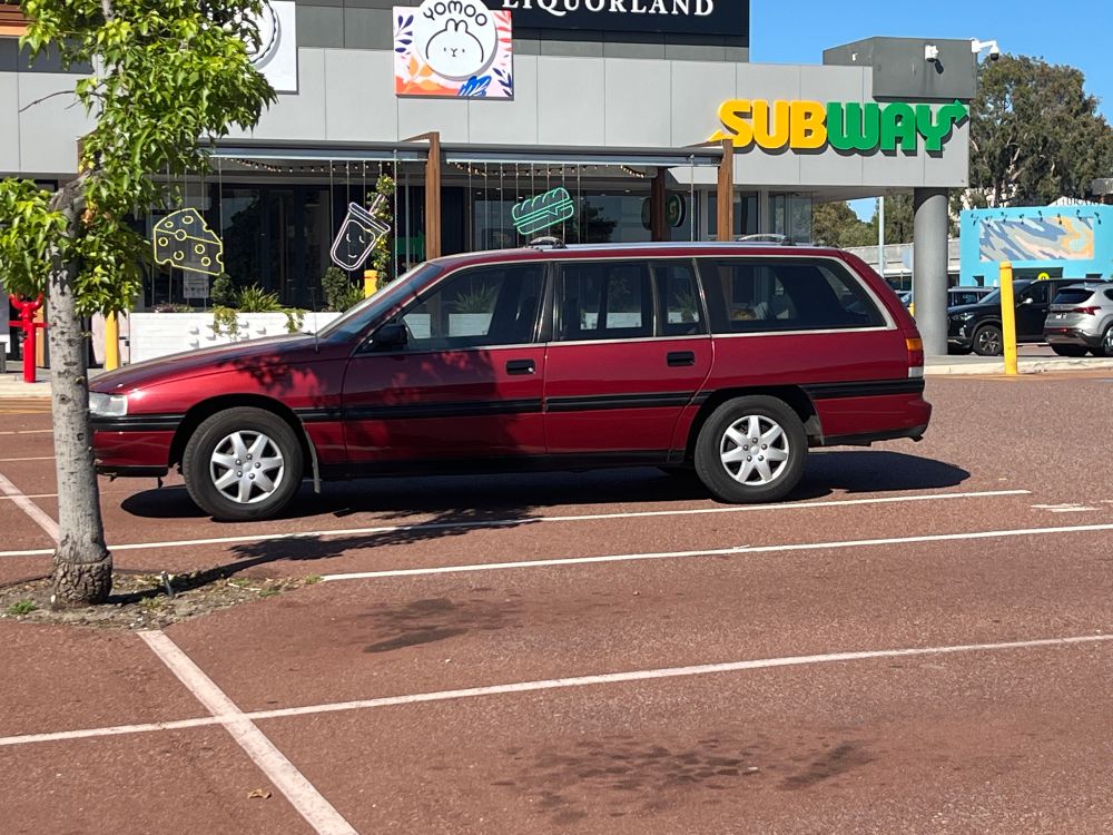 A red Holden VN Commodore wagon parked outside subway.