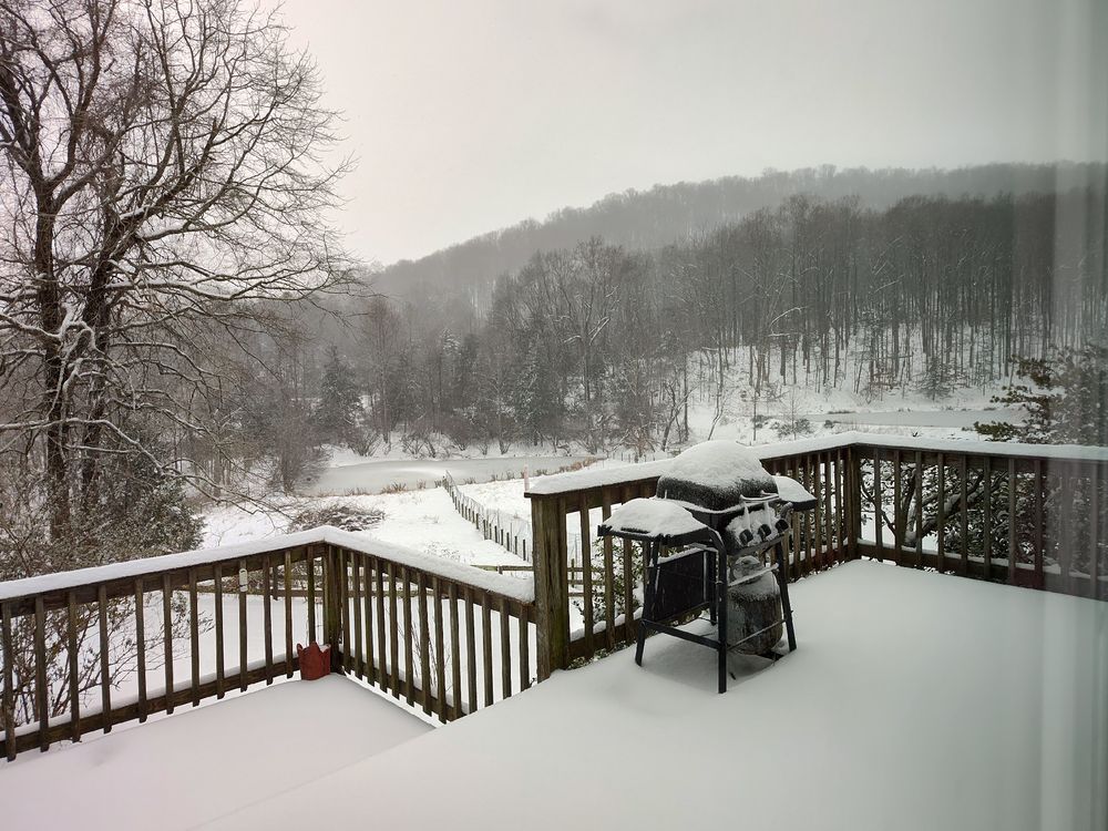 A deck covered in snow, with a view of a frozen pond and the mountains behind.