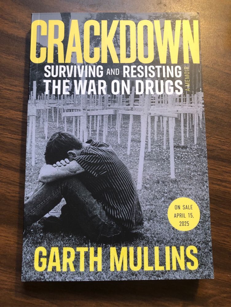 Picture of book: Crackdown by garth Mullins. Picture of a man sitting by many crosses. 