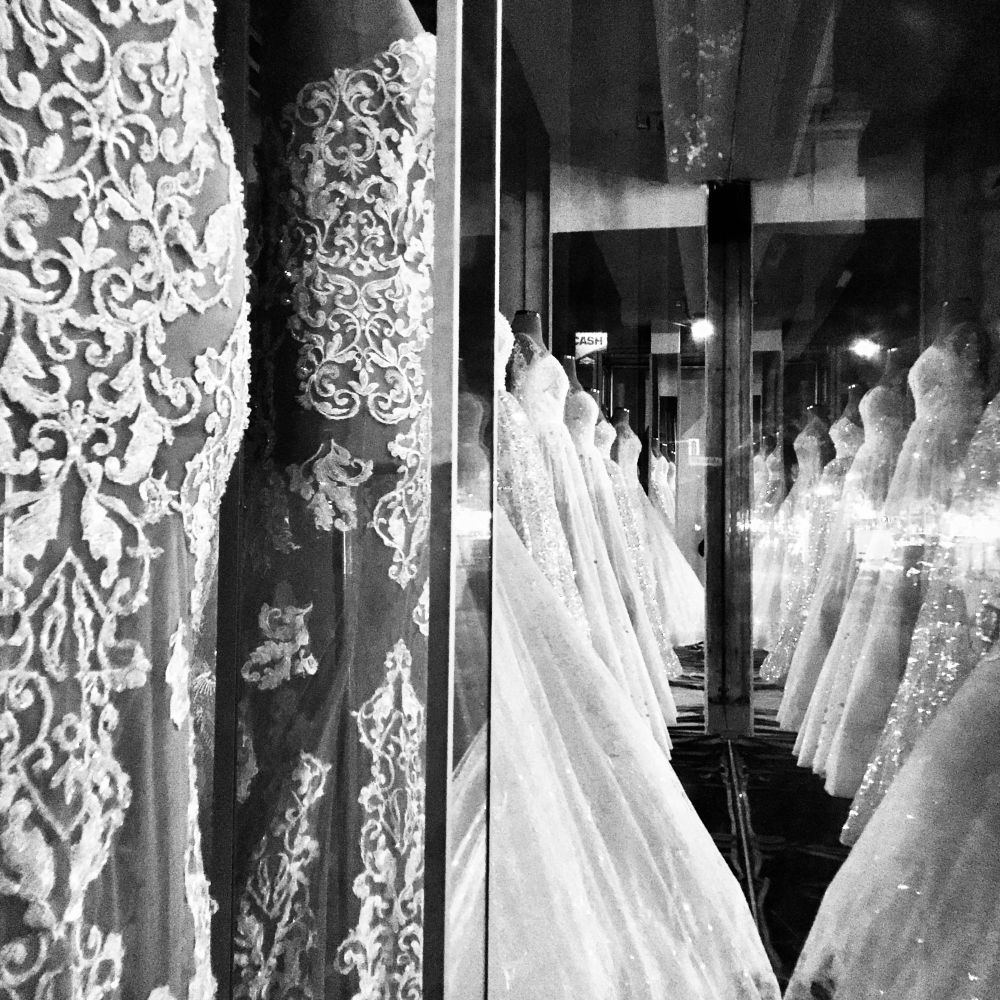 Schwarz-Weiß-Foto (Rohbild) mit der nächtlichen Innenaufnahme eines Brautmodengeschäfts, in dem sich durch das Fotografieren in Spiegelflächen die Brautkleider verdoppeln bzw. gegenüberstehen. 