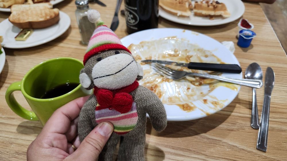 A stuffed monkey in front of an empty plate.
