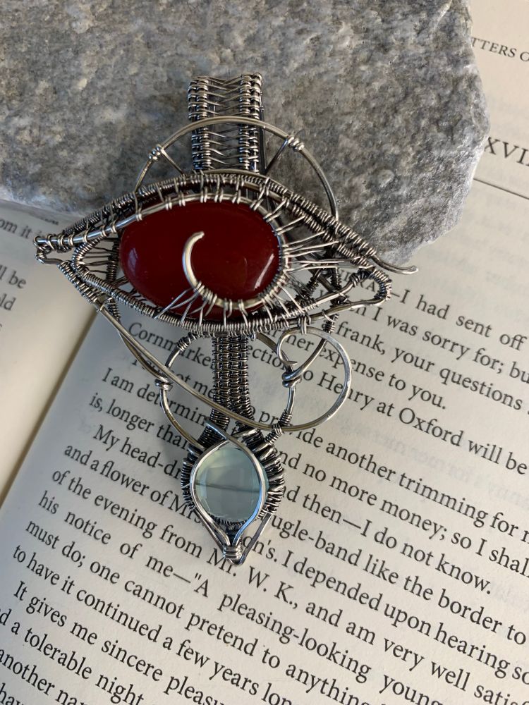 Sterling silver pendant. Wire woven carnelian eye of horus with a sweet aqua chalcedony below it. It's big and weird and gorgeous. Pictured below a rock holding open a book of the Letters of Jane Austen. 