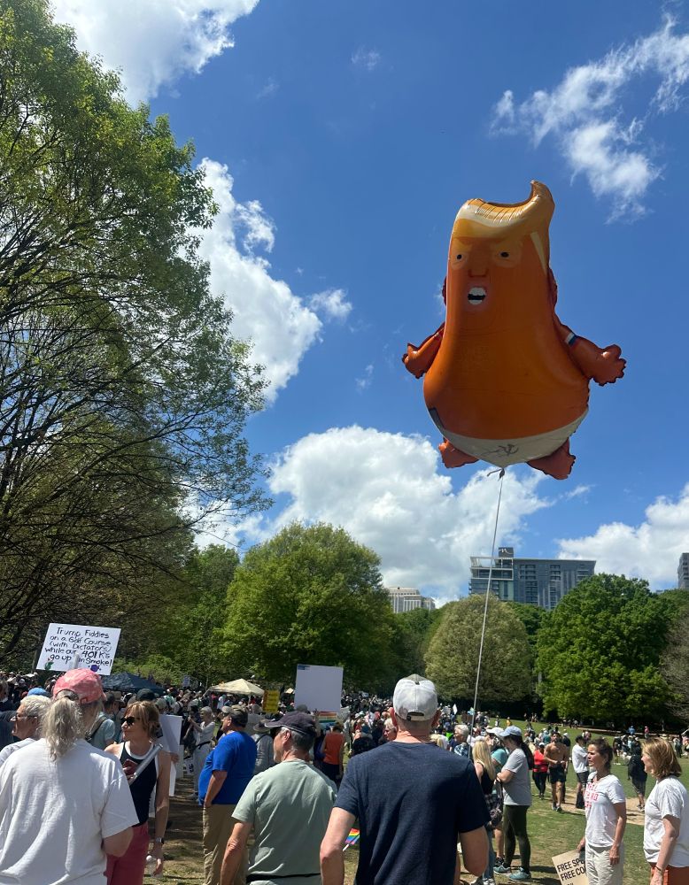 A cartoonish baloon of Trump flies above a crowd in a field in Atlanta