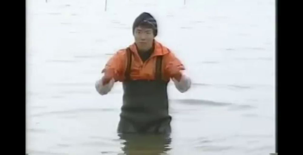 a man is standing in the water wearing an orange jacket and overalls .