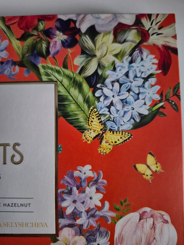 zoomed in pic of a box of chocolate candies from the top right side of it with a painting of flowers on red background 