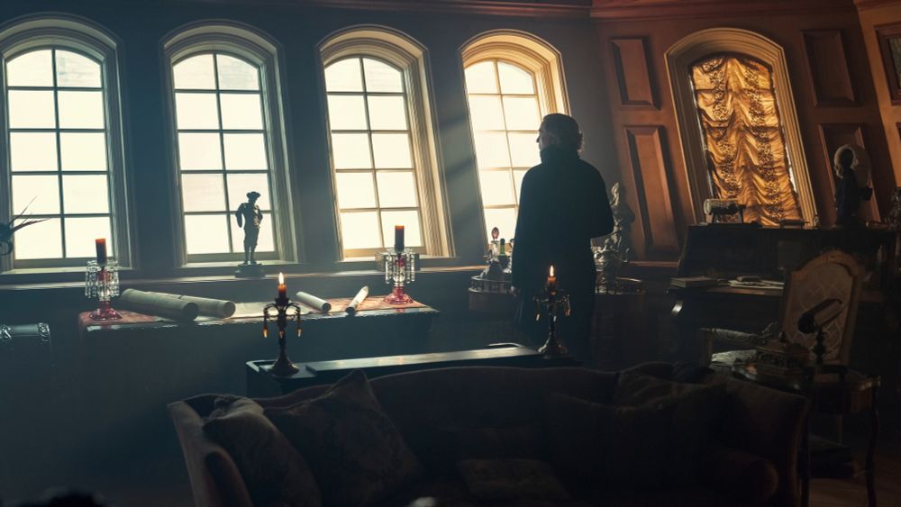 picture of Stede from OFMD season 1 episode 6, he's wearing black turtleneck, he'd standing in the distance back to the screen and is looking out of the windows