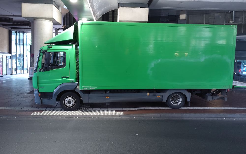 Ein grüner Lkw steht am Bahnhof Siegburg/Bonn auf dem Blindenleitstreifen und blockiert zusätzlich den abgesenkten Bordstein – eine klare Behinderung für Menschen mit Seh- oder Mobilitätseinschränkungen. Barrierefreiheit geht anders.