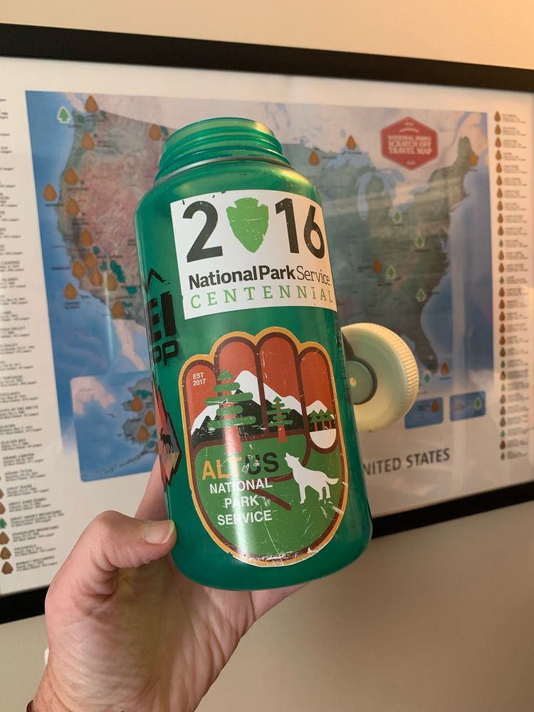 Green Nalgene water bottle with Alt US National Park Service sticker from the last time we went through this nightmare. In front of a National Park map showing all the parks I still need to visit. 