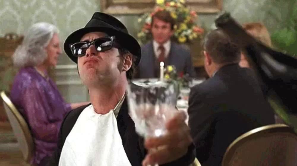 a man wearing a hat and sunglasses is holding a glass of wine