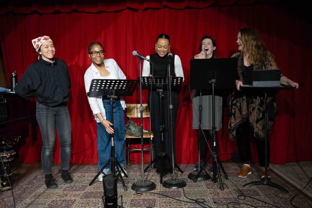 Five women laughing behind microphones and music stands