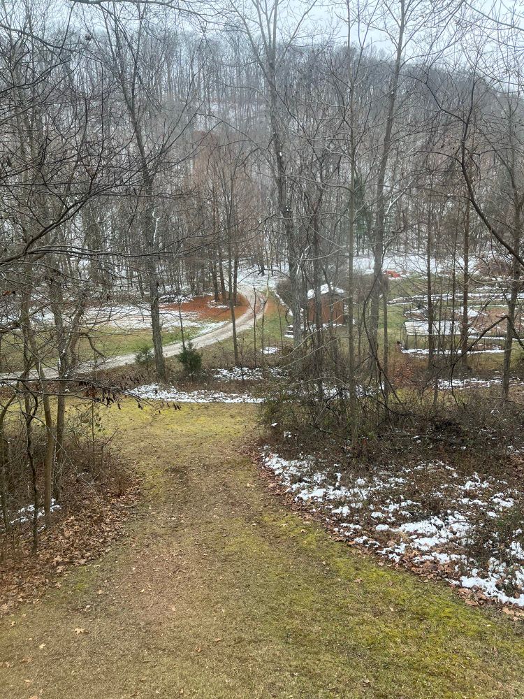 Photo from a window of a house, looking toward a snow-covered north-facing slopes from a still-green south-facing slope