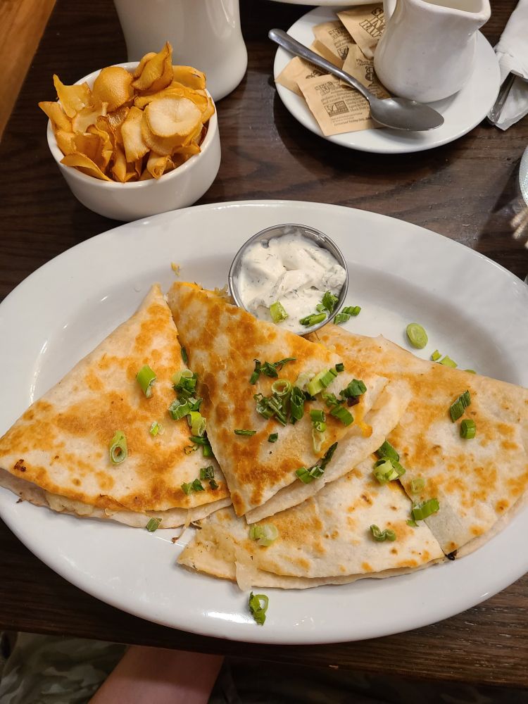Plate of vegan pierogi quesadillas topped with scallions, a side of vegan dill sour cream, and a bowl of yucca chips served at the Chicago Diner
