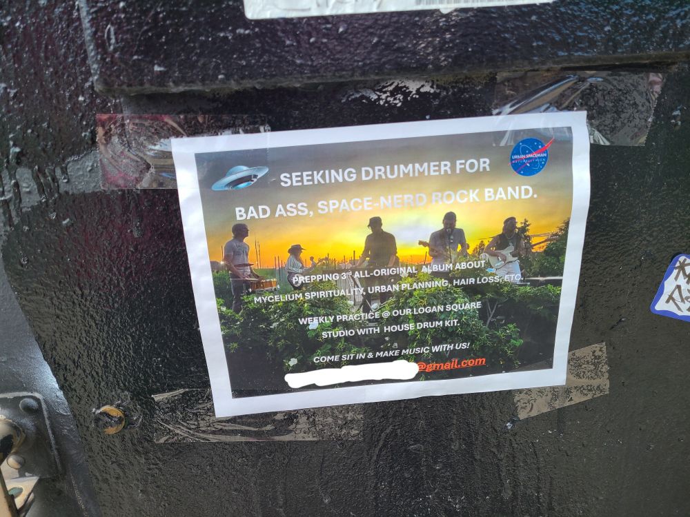 flyer posted on a streetlight that reads "SEEKING DRUMMER FOR BAD ASS, SPACE NERD ROCK BAND. PREPPING ALL-ORIGINAL ALBUM ABOUT MYCELIUM SPIRITUALITY, URBAN PLANNING, HAIR LOSS, ETC."