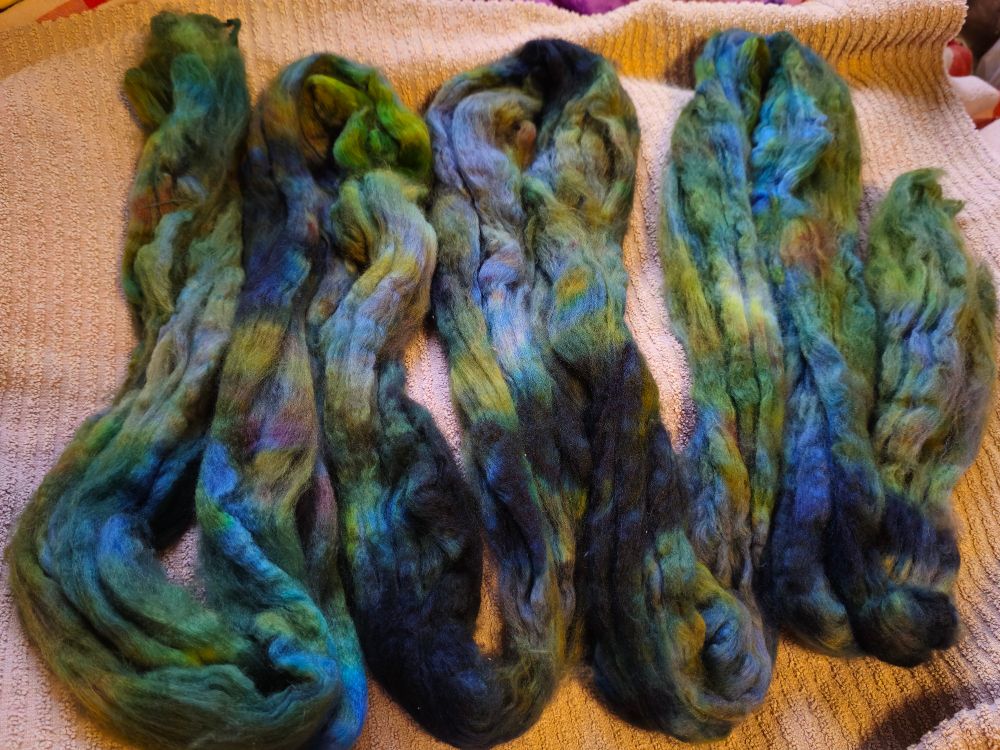 A photo of some hand dyed merino wool. It is in shades of green, blue, grey, and black.