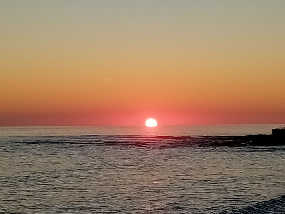 Red sun setting over the sea. The sky is vibrant shades of pink, red, and orange.
