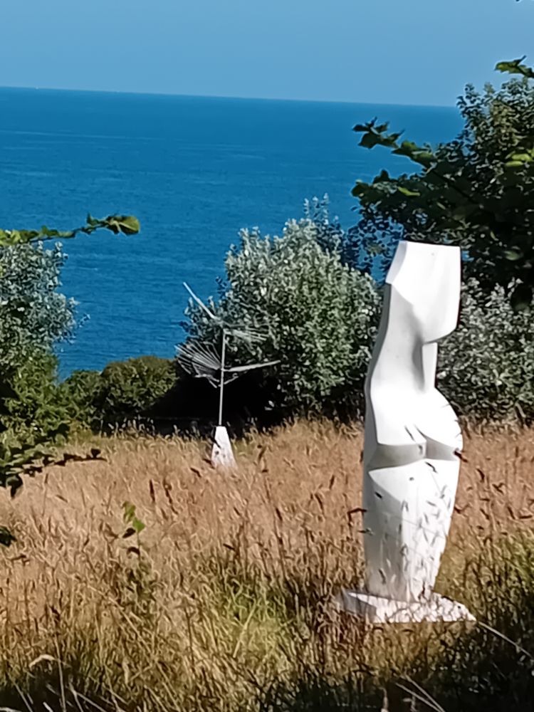 Two white sculptures in a sloping field of long grass overlooking the sea