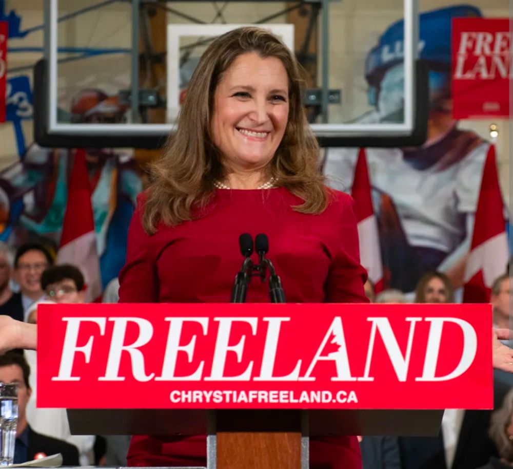 Chrystia Freeland standing at a podium in front of a placard with her campaign logo