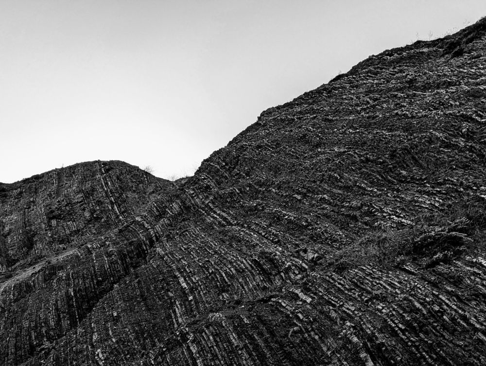 Diagonal, nearly vertical striations of sedimentary rock on the side of a mountain that's been cut into for a road