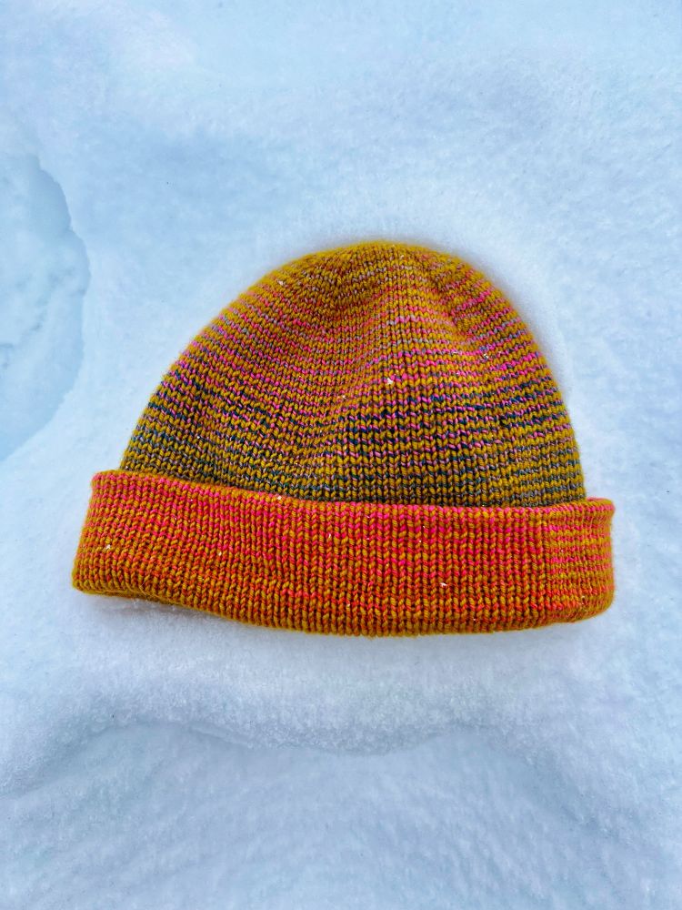 A brightly colored hand-knit Musselburgh hat lays on a bed of fresh snow in Southern Oregon. 