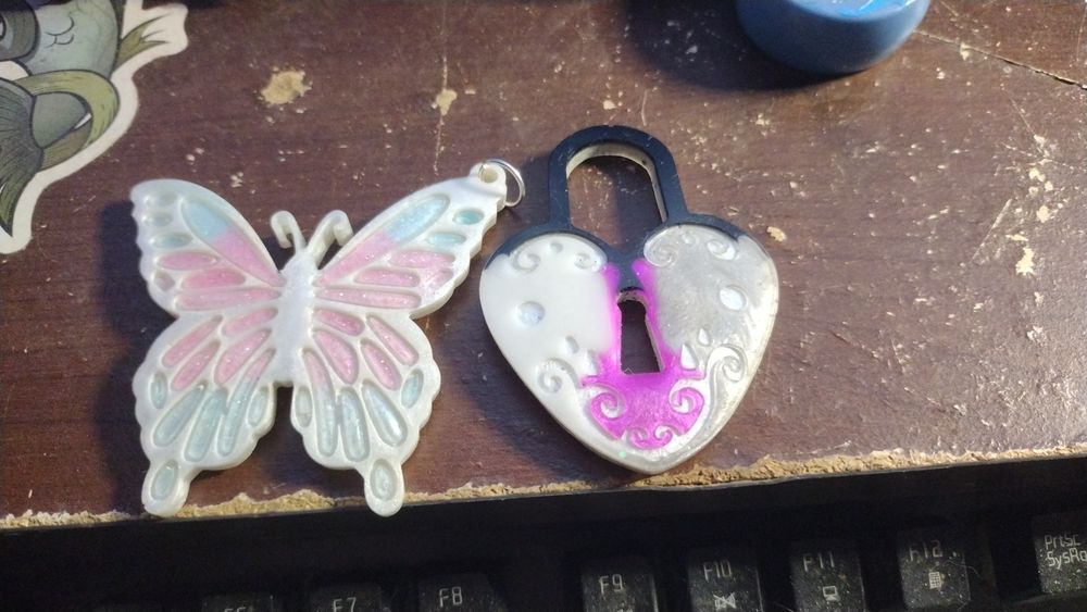 A white, blue, and pink resin butterfly and a black, grey, white, and purple resin hear padlock