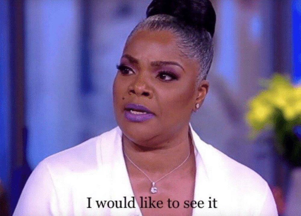 A reaction image of a woman looking off-camera, as though speaking to someone in an interview setting. She looks very serious and the caption reads, “I would like to see it.”