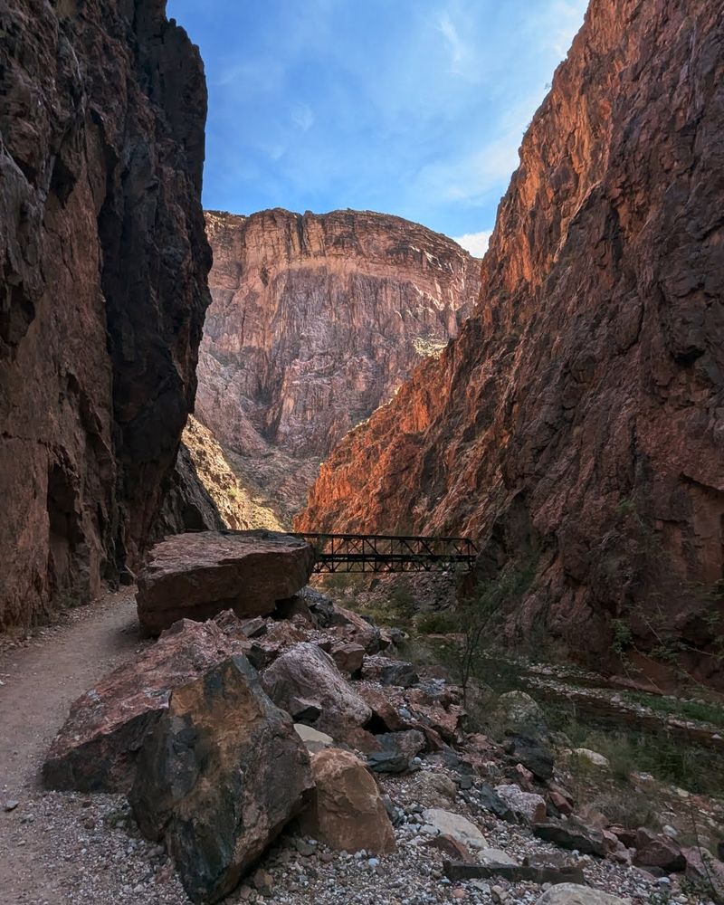 Inside the canyon on trail with red rocks rising around, and a bridge up ahead to cross the colorado river, which is narrowed here