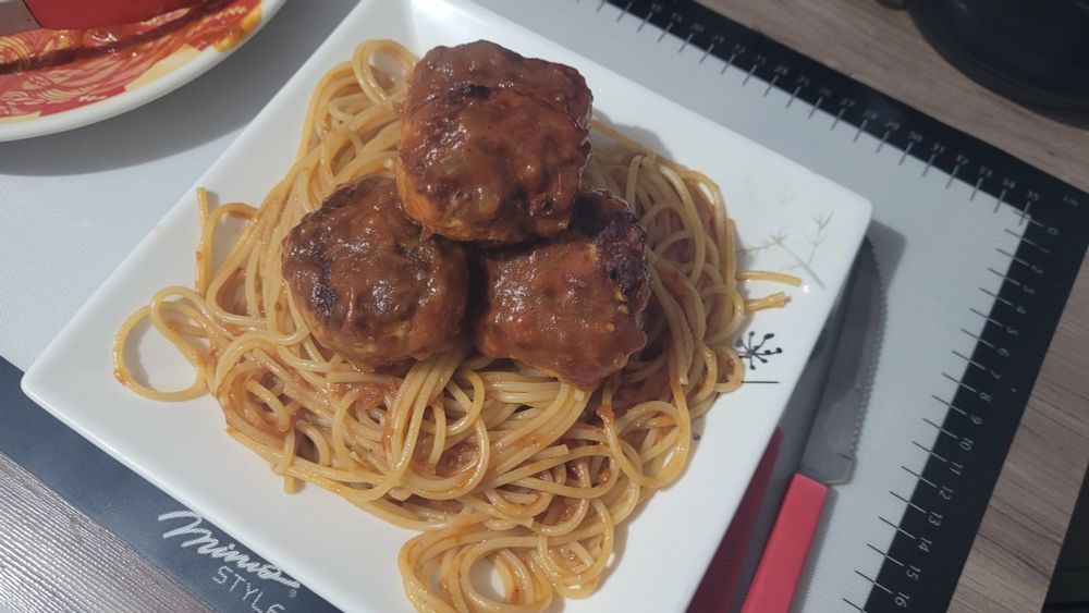 Um prato quadrado com espaguete ao molho de tomate e com 4 almôndegas em cima