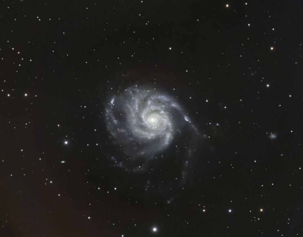A spiral galaxy fills the center third of the image. Several bright arms spiral away from a very bright core. The spiral arms are distorted by the gravity of other nearby galaxies. The galaxy is set against a field of dimmer stars.