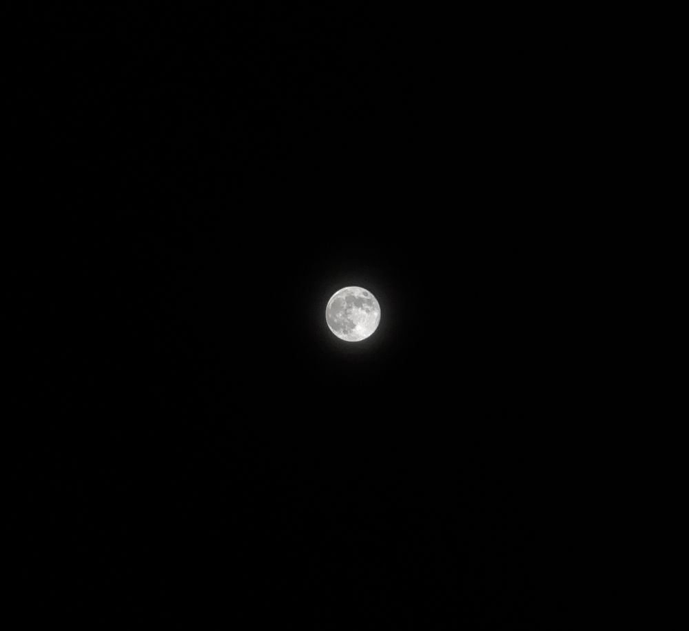 The full moon in the center of the image, dimmed a little by thin clouds.
