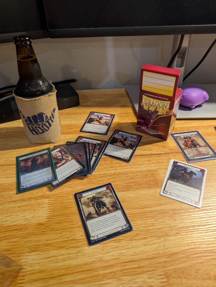 Flesh and Blood cards for the deck of Kassai of the Golden Sand on a desk with a beer in a Hootie & the Blowfish coozie 