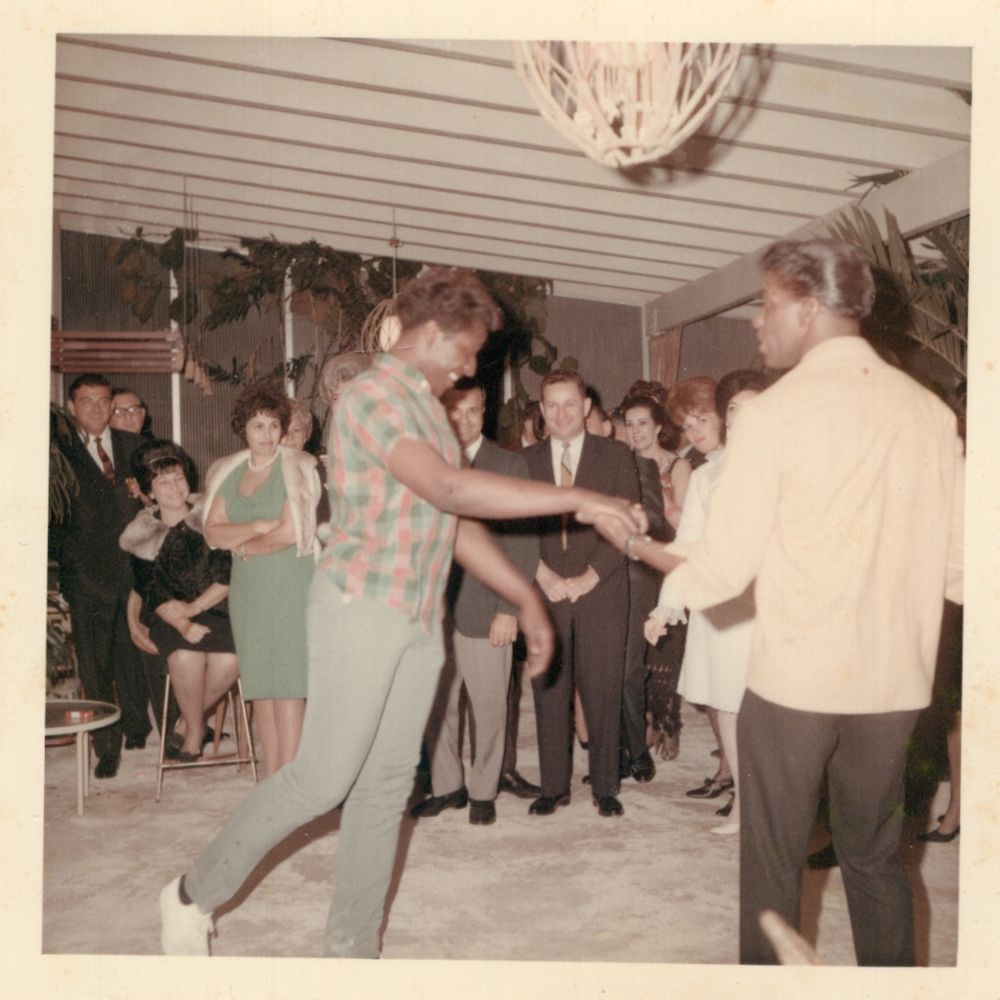 Two Black men dancing at a party full of white people