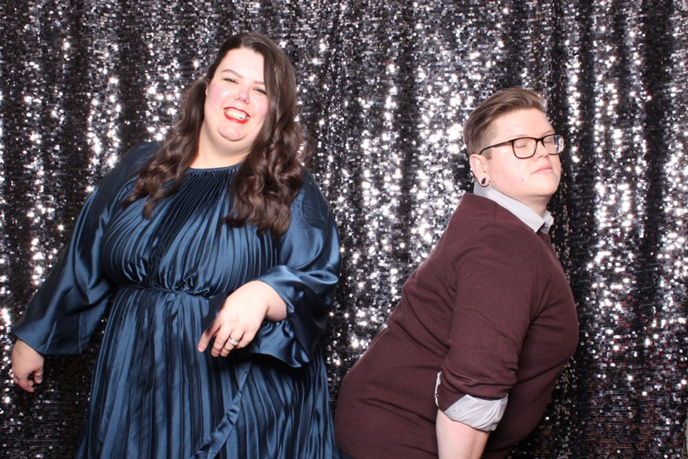 Cait and her husband, dressed up at a holiday party, pose in front of a silver sequined backdrop 