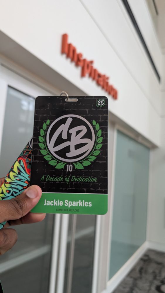 A Black dude who still bites his fingernails occasionally holds up a black and green lanyard. On it, it contains a circular "CB" logo, adorned with leaves. Below the seal, it reads: 

"10"
"A Decade of Dedication"

Below that is the OP's tag, Jackie Sparkles. He says hi. 

To the upper right, a "25" is seen. 