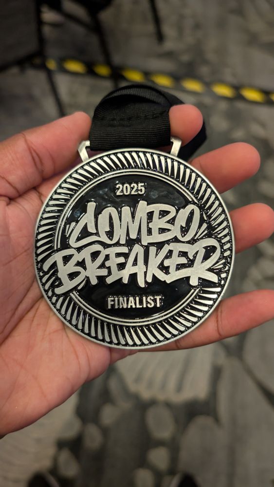 A hand holds a silver and black medal. On it, from top to bottom, read the following:

"2025
COMBO
BREAKER
FINALIST"