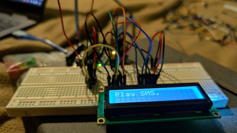 A breadboard, a whole lot of wires, and a LCD screen that says "Play SMS."